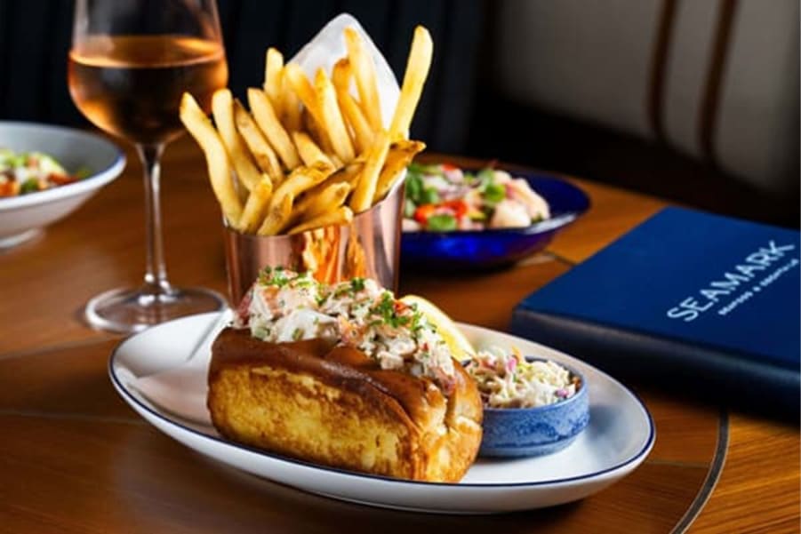 Lobster roll served with french fries, coleslaw, and a glass of white wine on a restaurant table