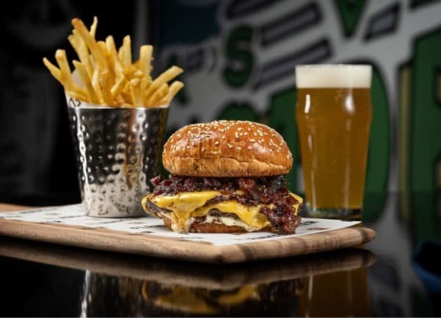 Cheeseburger with crispy bacon served with French fries and a pint of beer on a restaurant table.
