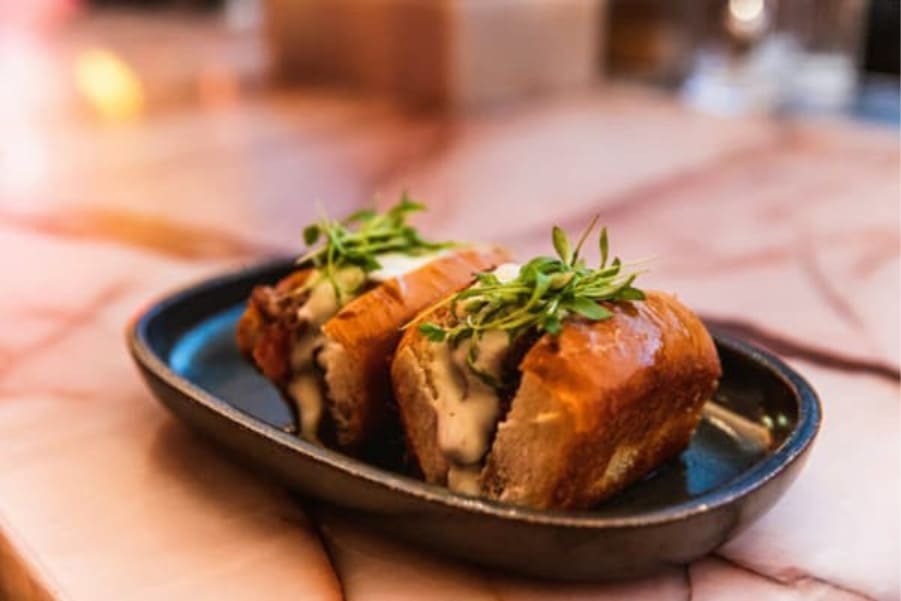 Gourmet slider sandwiches served on a black plate with melted cheese and fresh herbs garnish