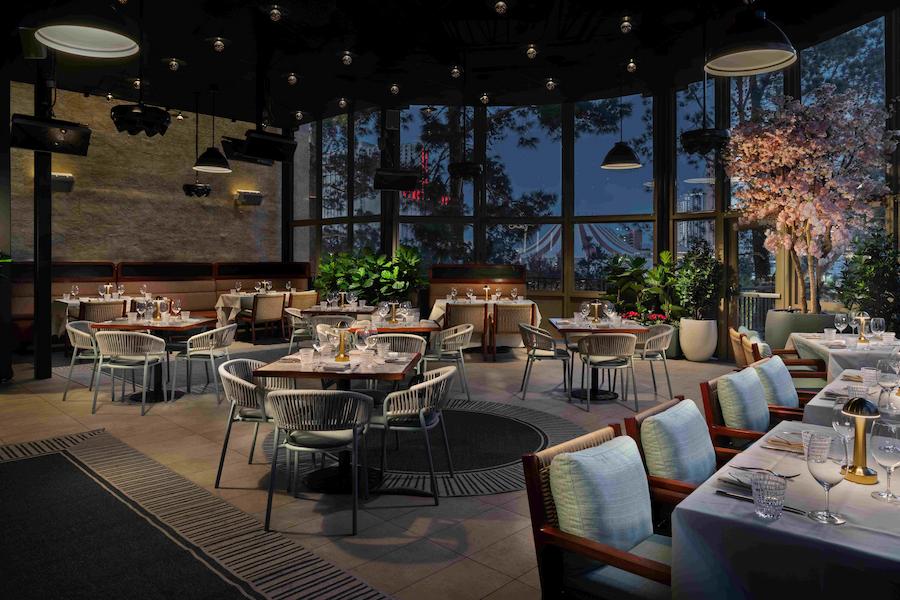 Elegant outdoor patio dining area at Carversteak featuring beautifully set tables, cushioned seating, lush greenery, and ambient evening lighting in a modern open-air restaurant setting.