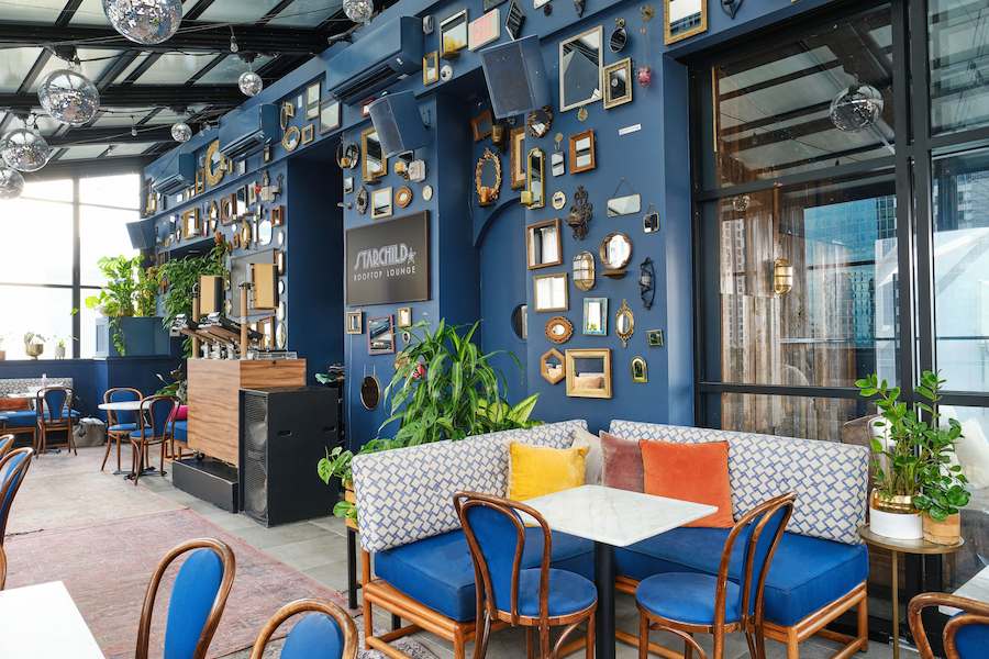 Starchild Rooftop Lounge interior with blue seating, colorful accent pillows, greenery, mirrored wall décor, and hanging disco balls.